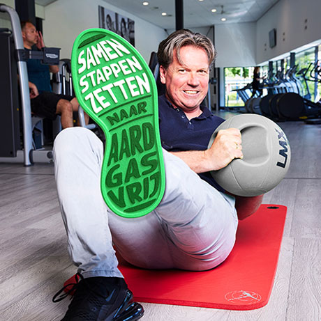 Man in de sportschool met sportbal en een schoenzool met 'Samen stappen zetten naar Aardgasvrij'.